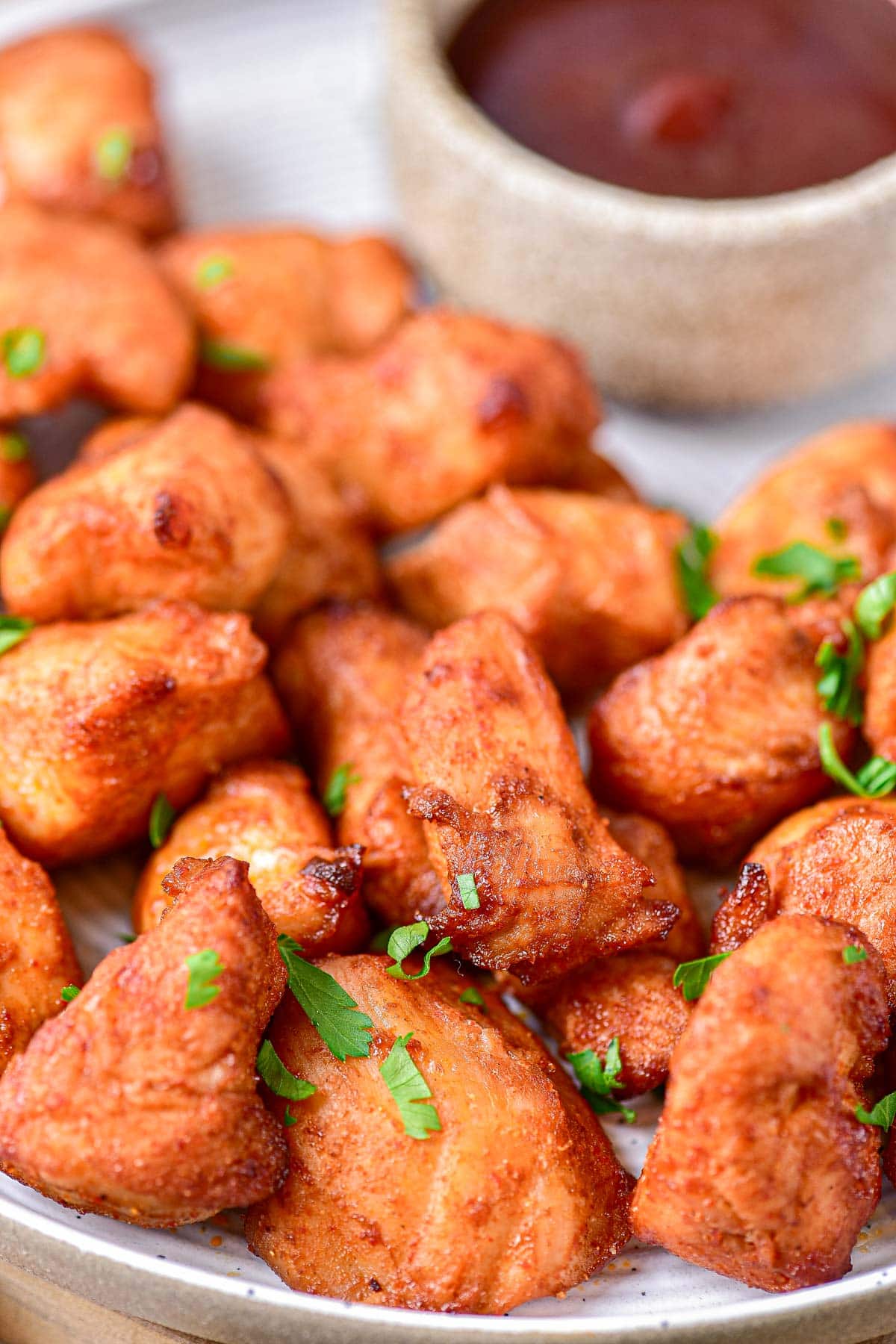 pieces of cooked marinated chicken on plate with sauce behind and parsley on top.