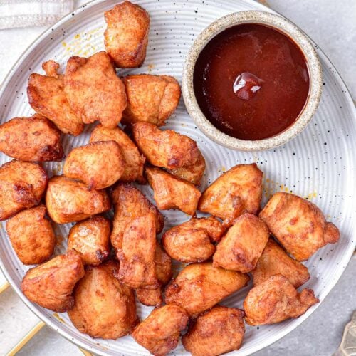 plate with chicken bites on it beside smaller bowl of dipping sauce.