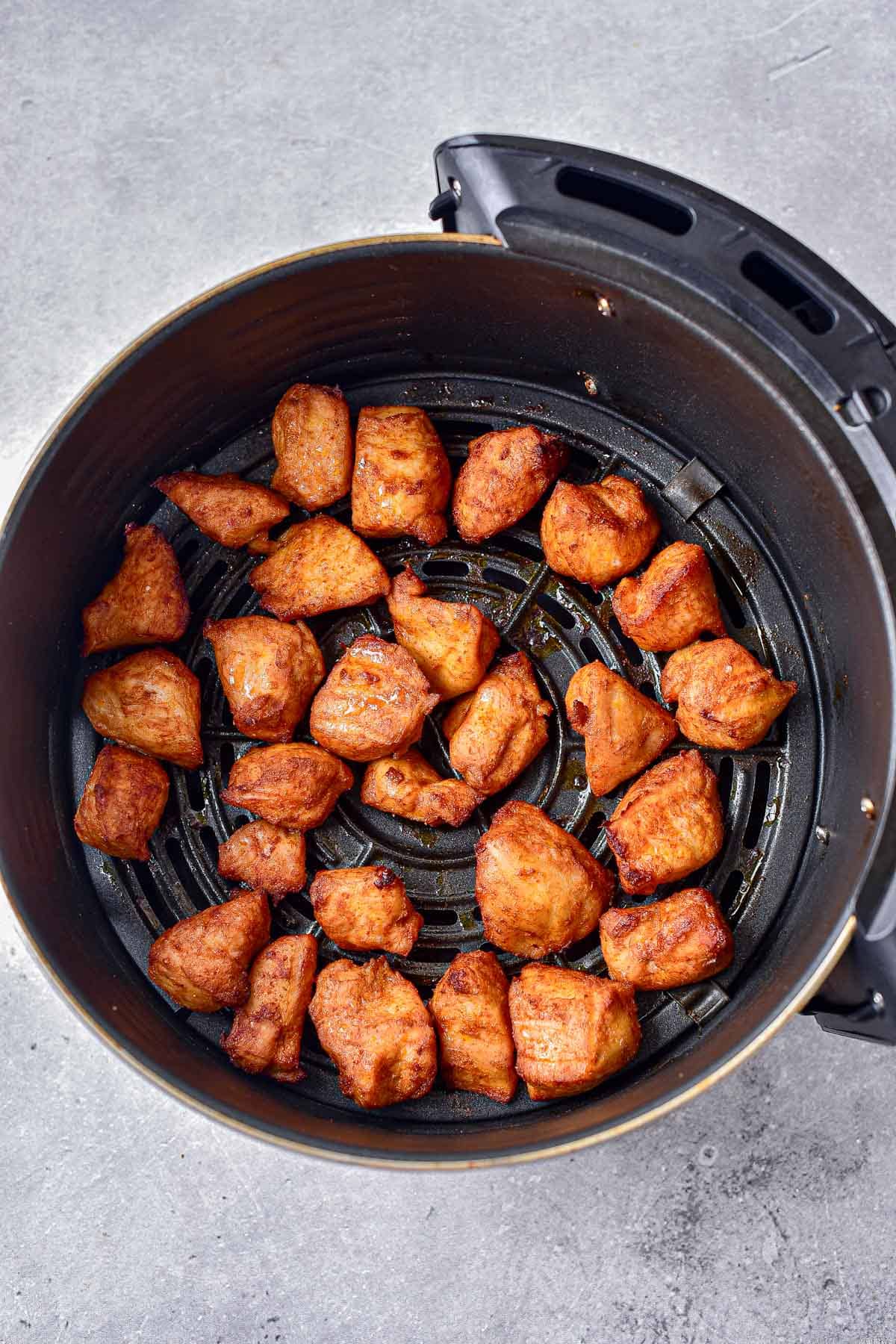 crispy chicken bites in round black air fryer tray sitting on counter.