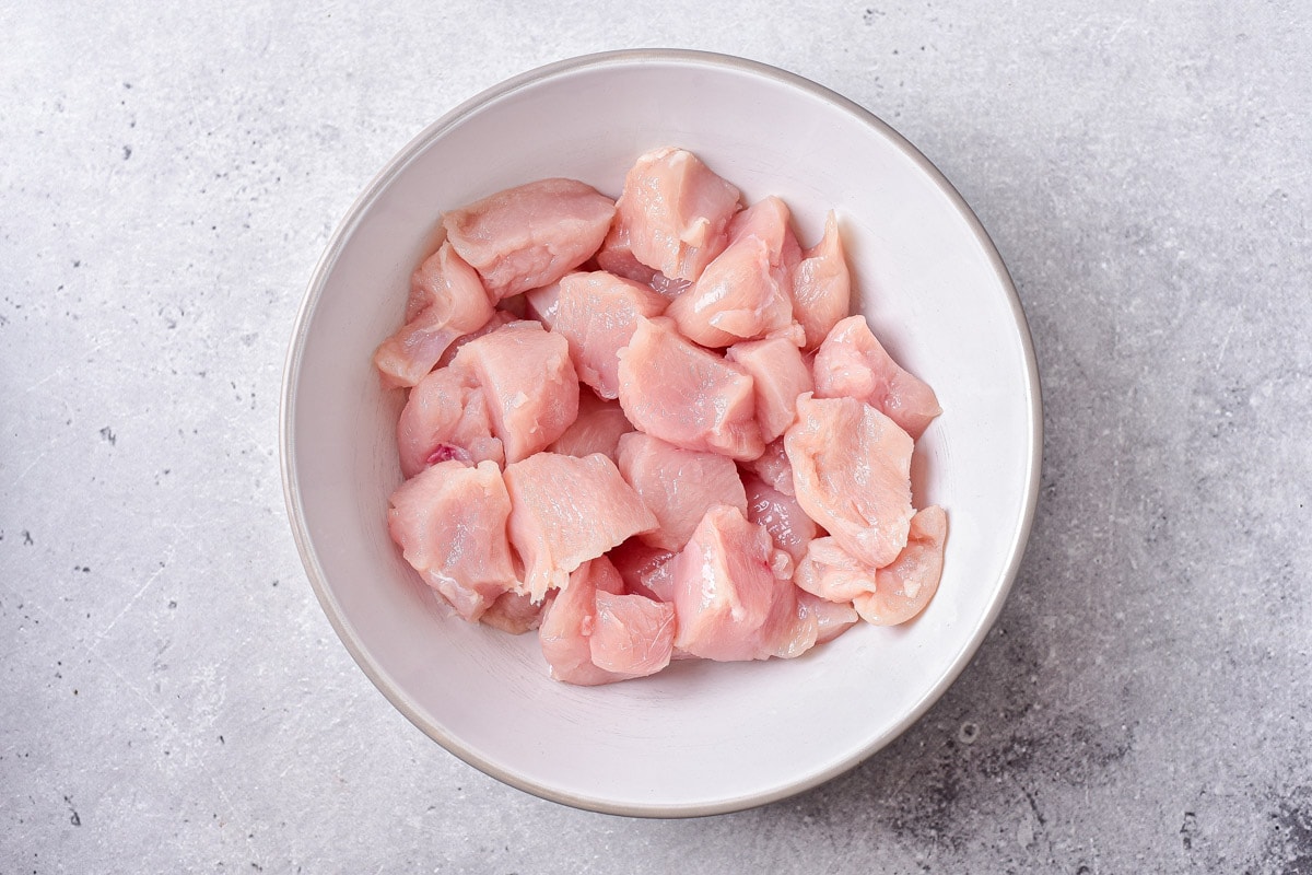 pieces of chicken breast cut up in white bowl on counter.