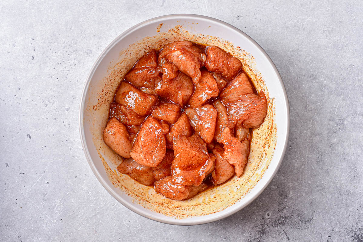 raw pieces of chicken covered in seasonings in white bowl sitting on counter.