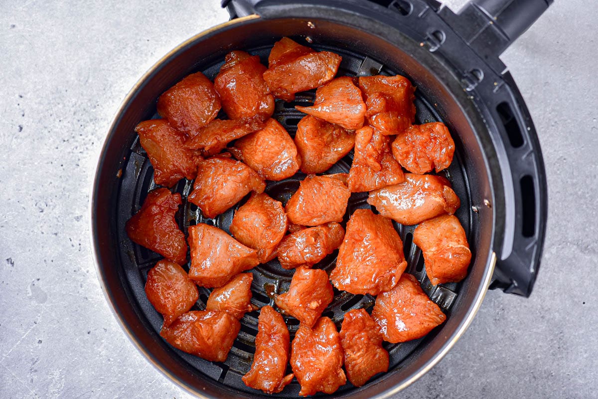 raw seasoned chicken pieces in round black air fryer tray on counter.