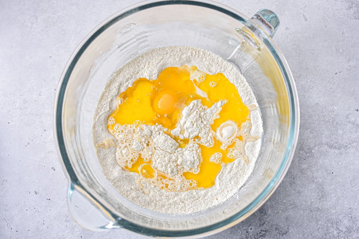 glass bowl with flour and raw egg inside sitting on counter.