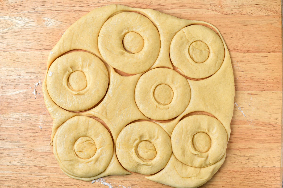 raw dough rolled out on wooden cutting board with donut shapes cut out.