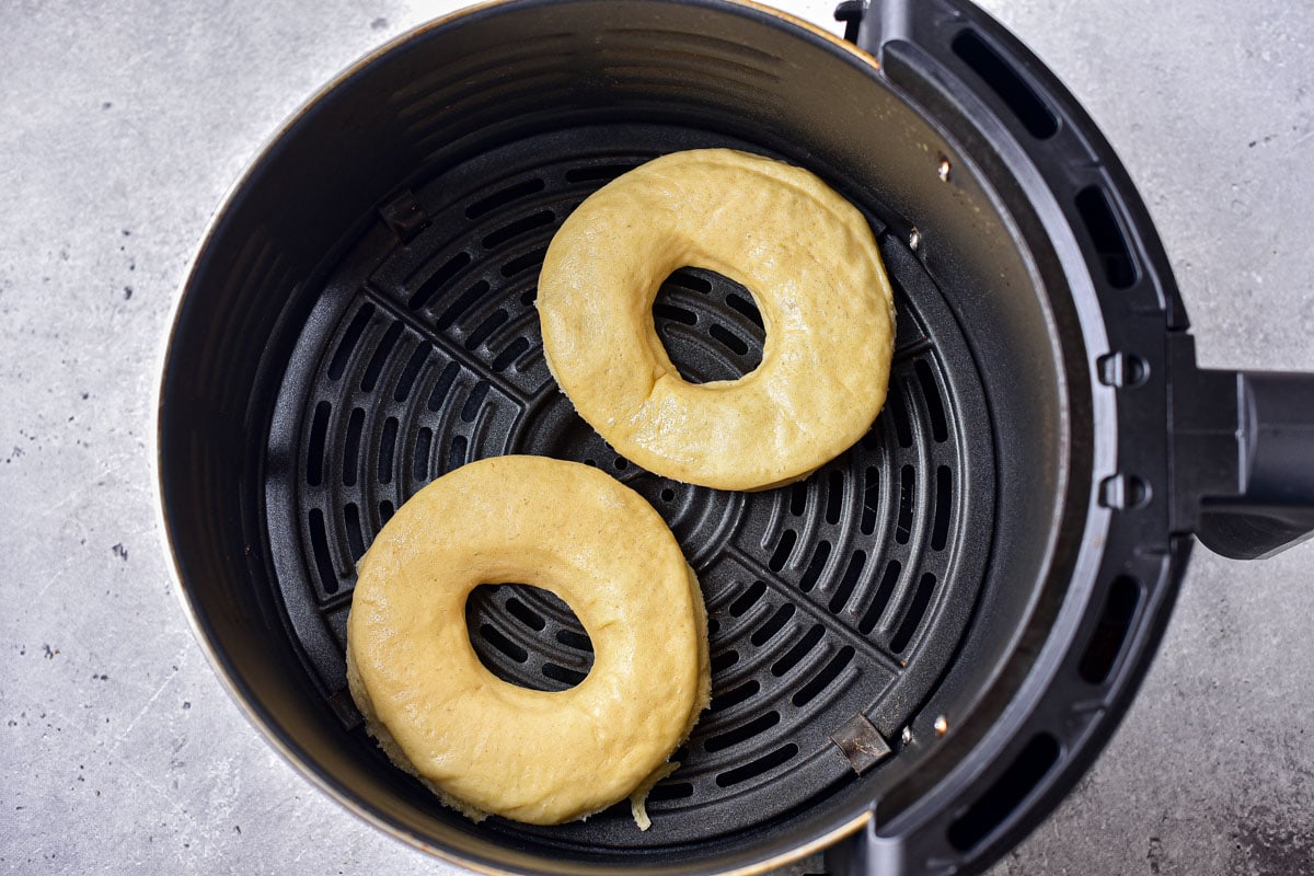 two raw donuts in round black air fryer basket.