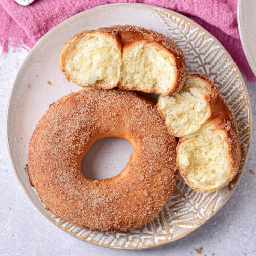 whole donut seen from top down on plate beside two halves of a ripped donut.