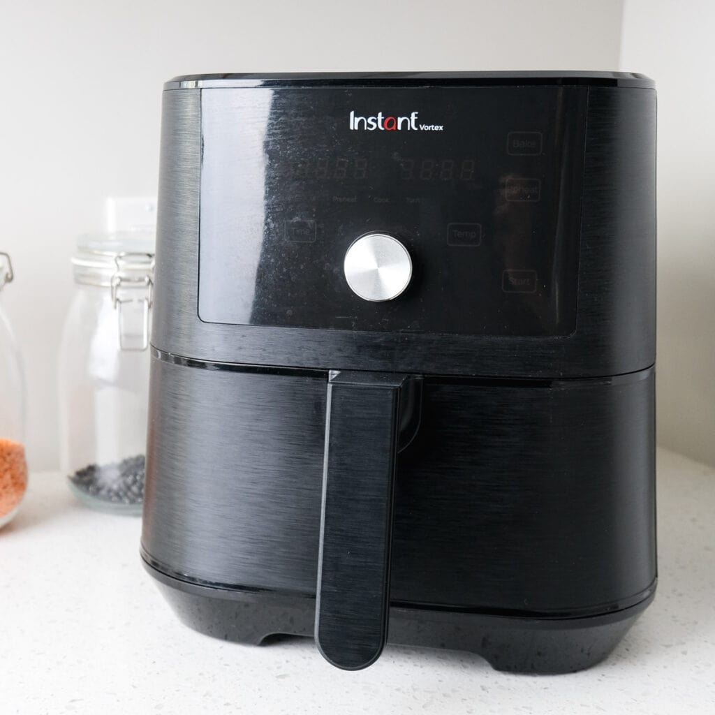black vortex air fryer on white counter with glass jar beside.