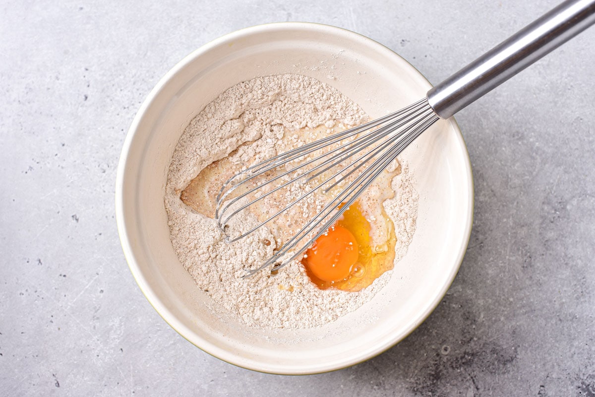silver whisk mixing ingredients in white mixing bowl on counter.