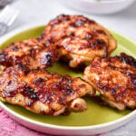 four bbq chicken thighs on green plate with forks behind.