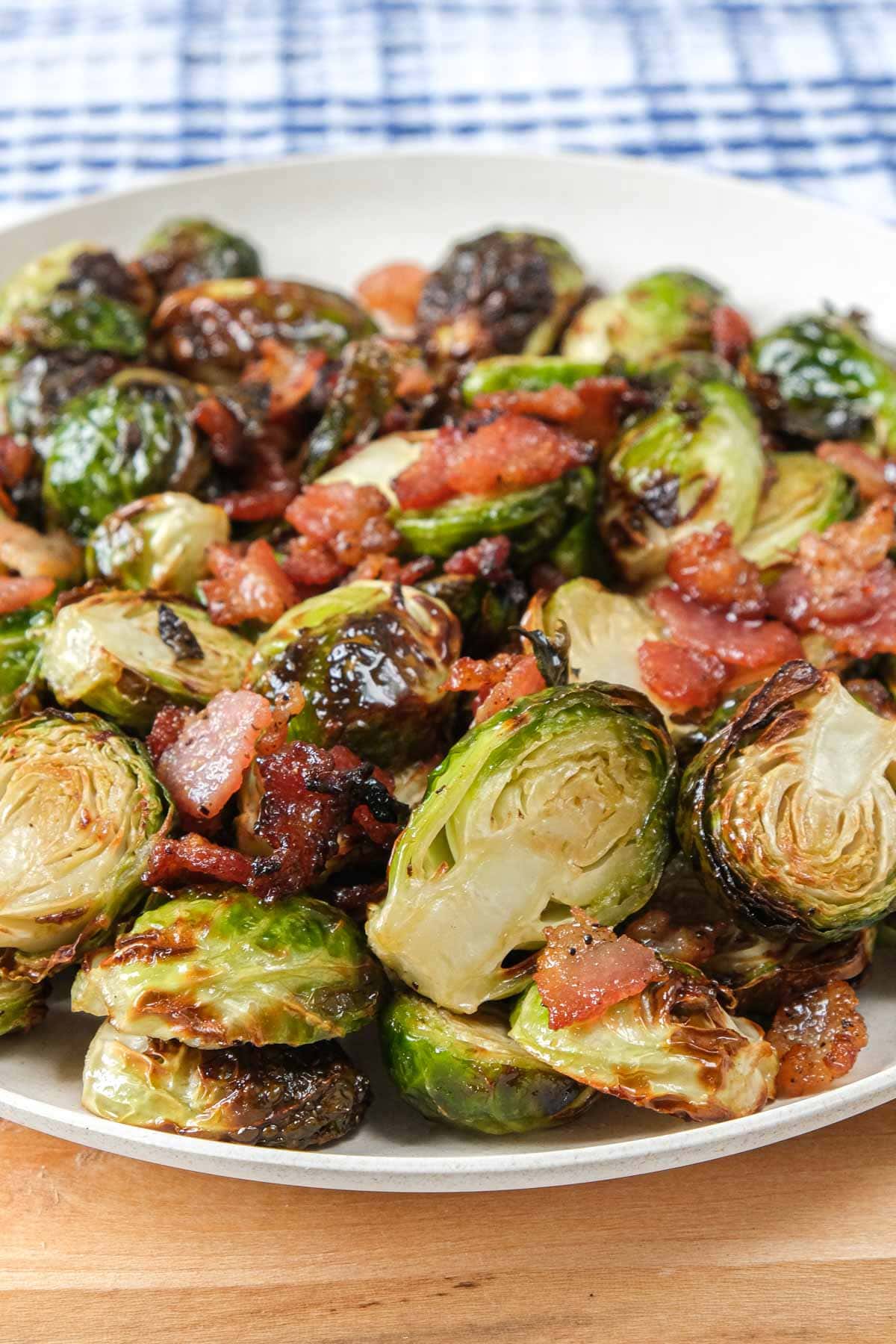 cooked brussels sprouts with bacon pieces on white plate on wooden board.