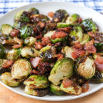brussels sprouts on white plate with bacon on wooden board.