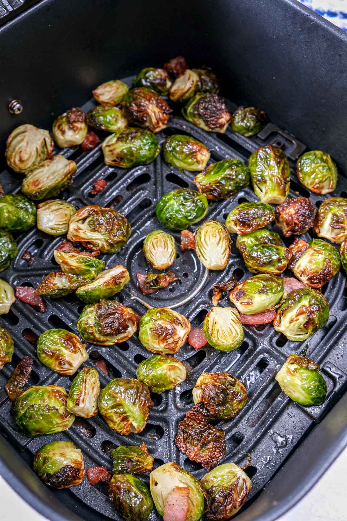 cooked brussels sprouts with bacon in black air fryer tray on counter.
