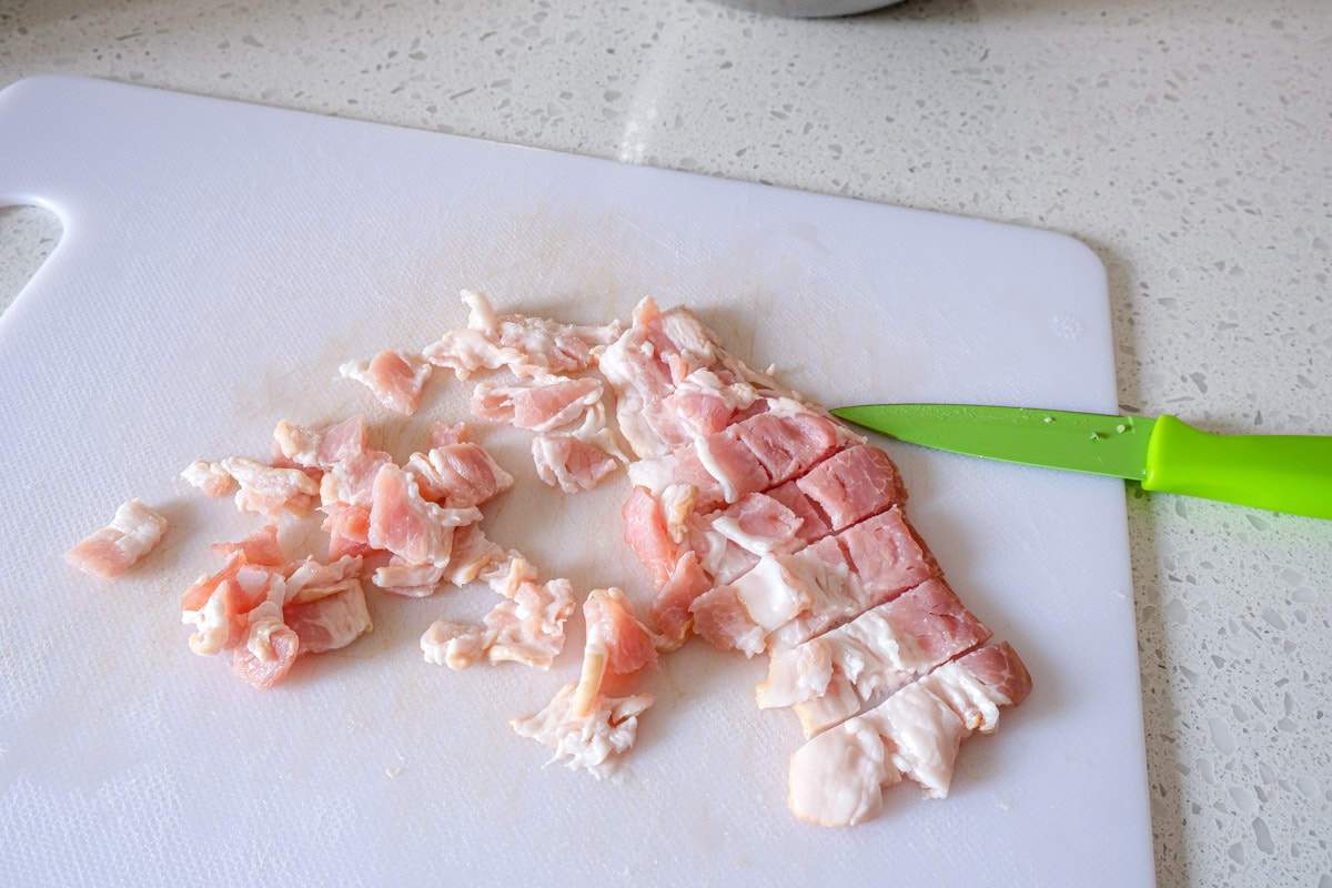 slices of bacon cut into smaller piece on white cutting board with knife beside.