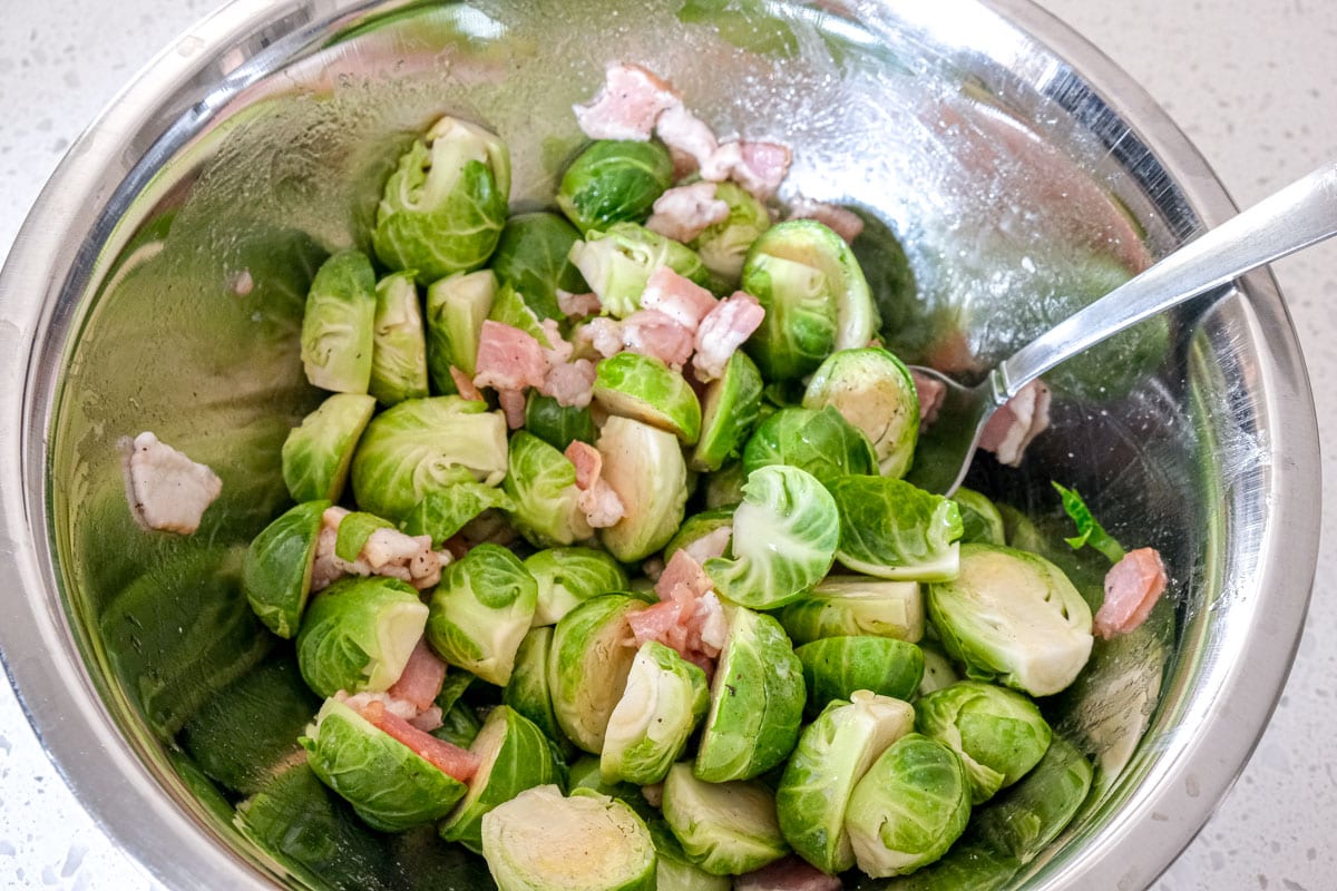 bacon and brussels sprouts mixed together in silver bowl with spoon on counter.