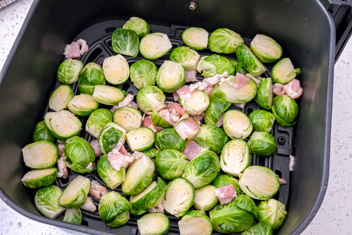 cut brussels sprouts with bacon in black air fryer tray.