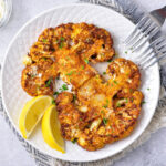 two crispy cauliflower steaks on white plate with two forks beside.