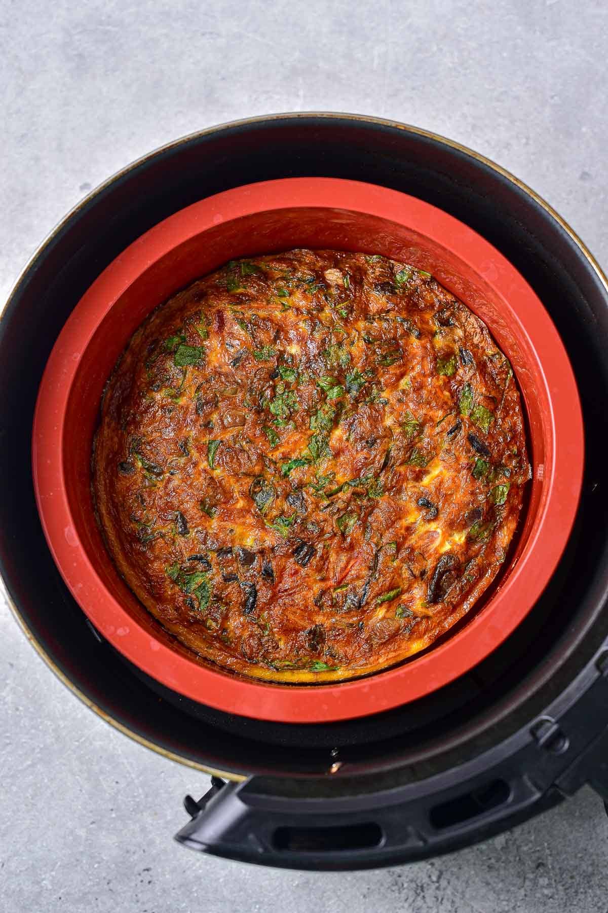 cooked frittata in red silicone pan in round air fryer basket.
