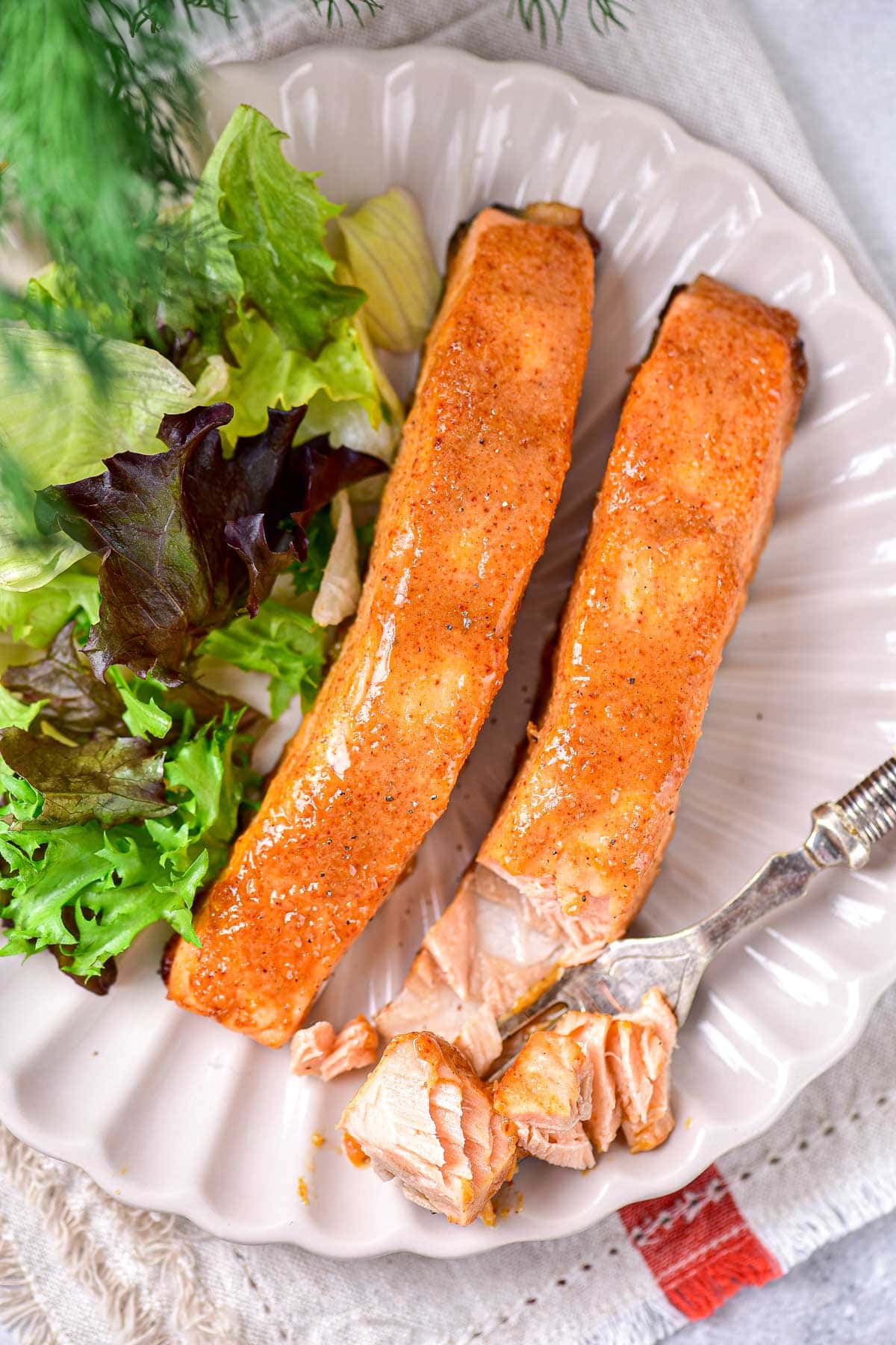 two pieces of honey mustard salmon on plate with salad beside and fork flaking some salmon off.
