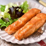 two fillets of honey mustard salmon on white plate with salad beside.