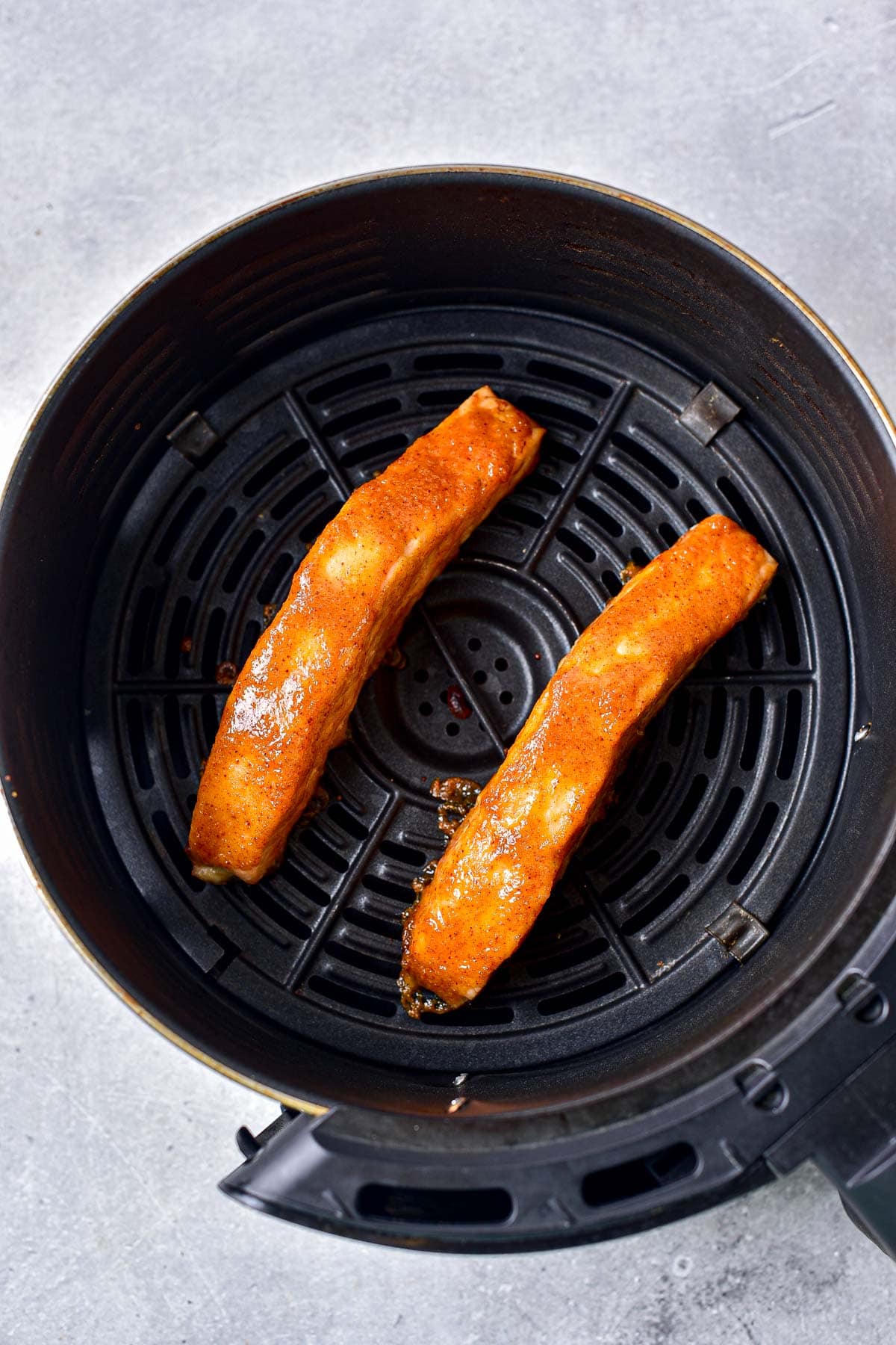 cooked pieces of honey mustard salmon in round black air fryer basket.