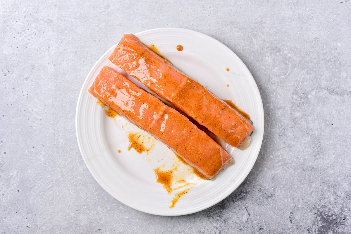two fillets of salmon glazed in marinade on white plate.