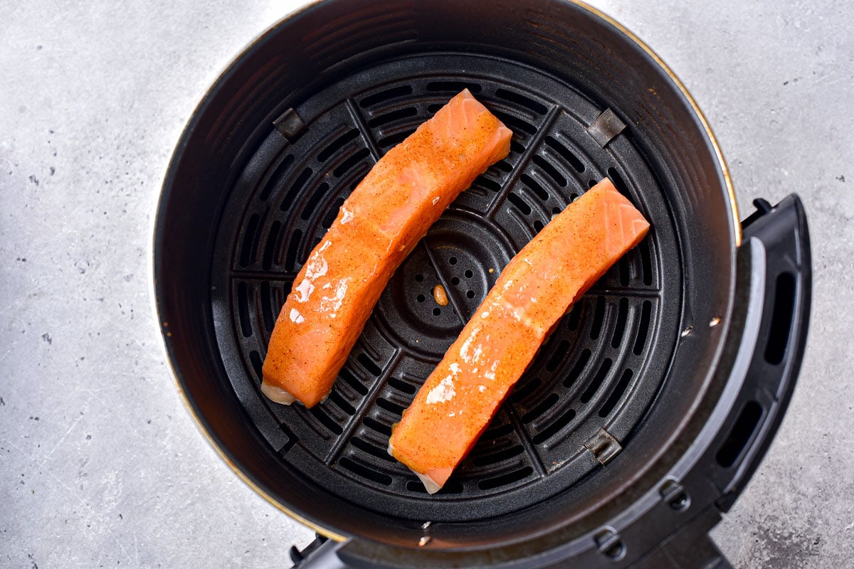 two marinated pieces of salmon in round black air fryer tray.