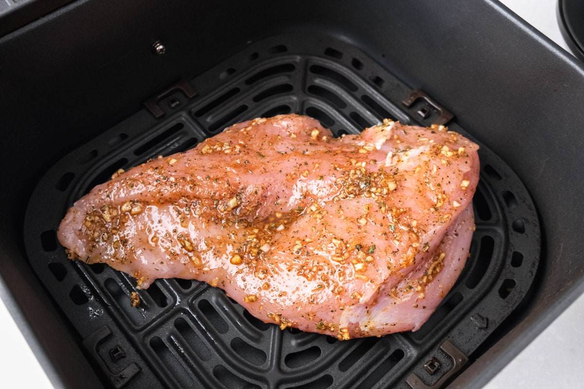 raw turkey breast covered in spices laying in black air fryer basket.