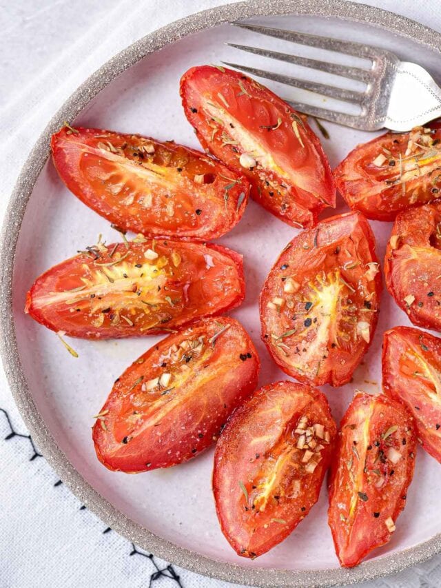 roasted tomato wedges on grey plate with silver fork beside.