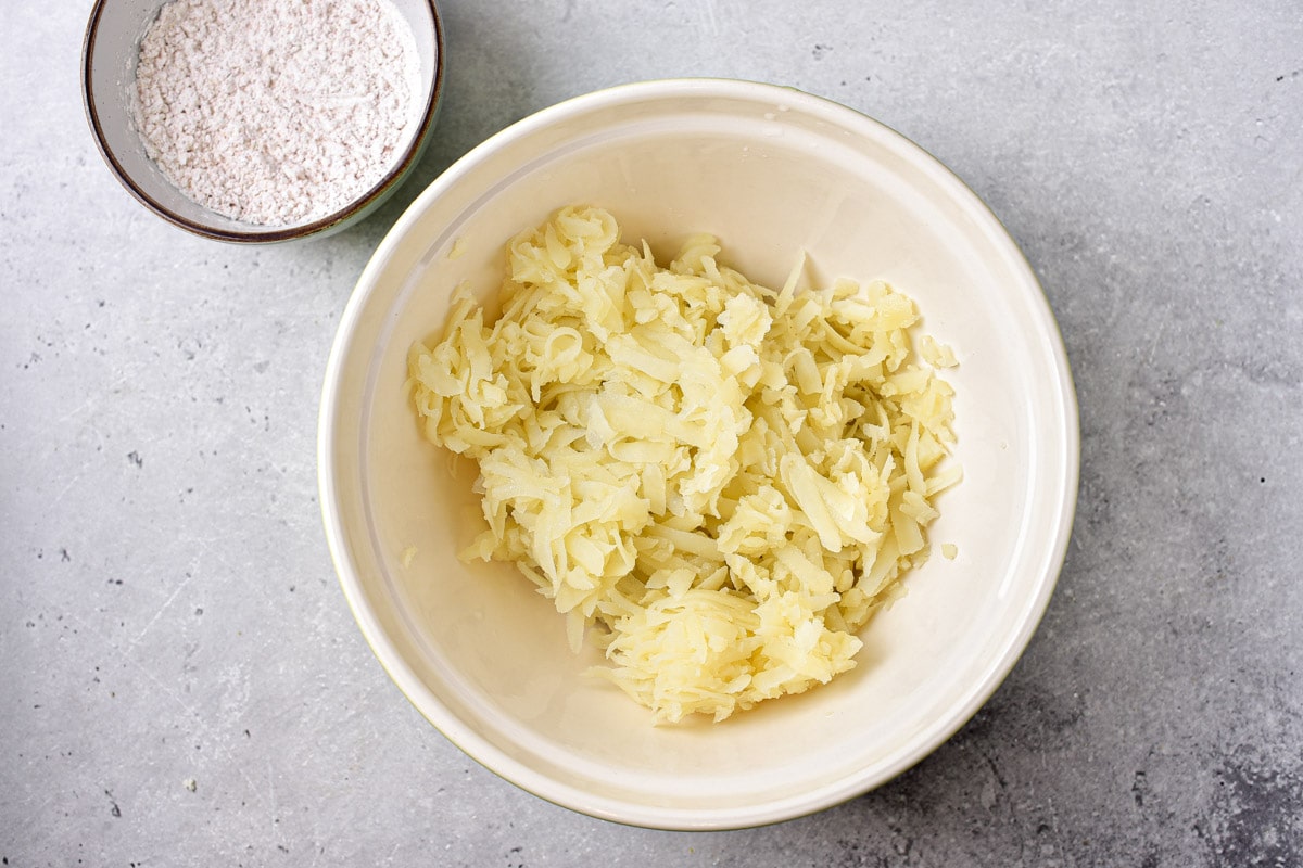 semi-cooked shredded potato in white mixing bowl.