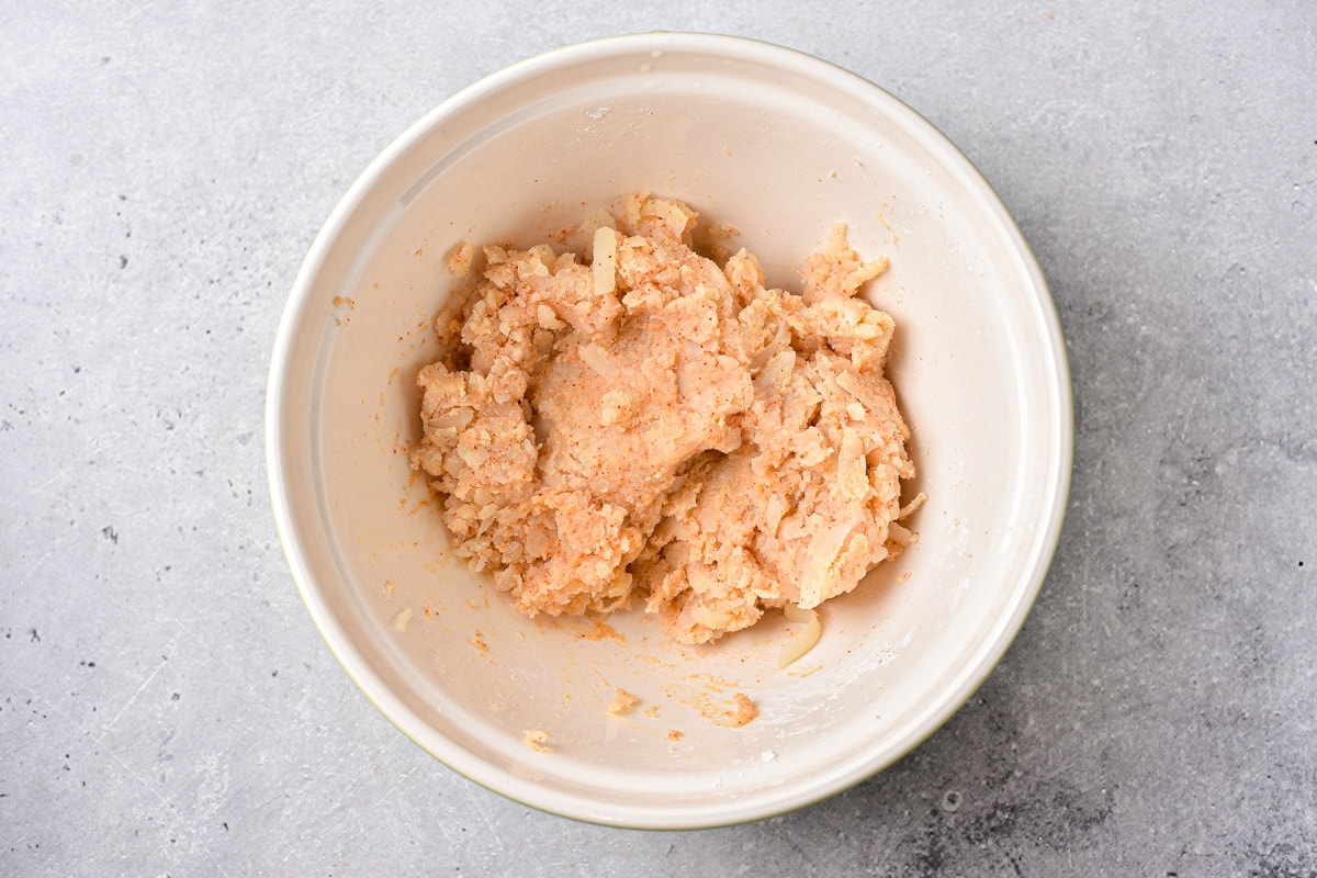 semi-cooked potato with spices in white mixing bowl on counter.