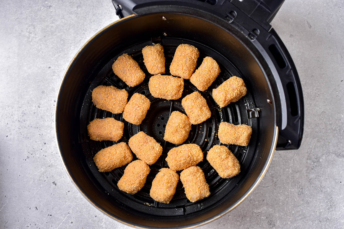 raw homemade tater tots in round black air fryer basket on counter top.