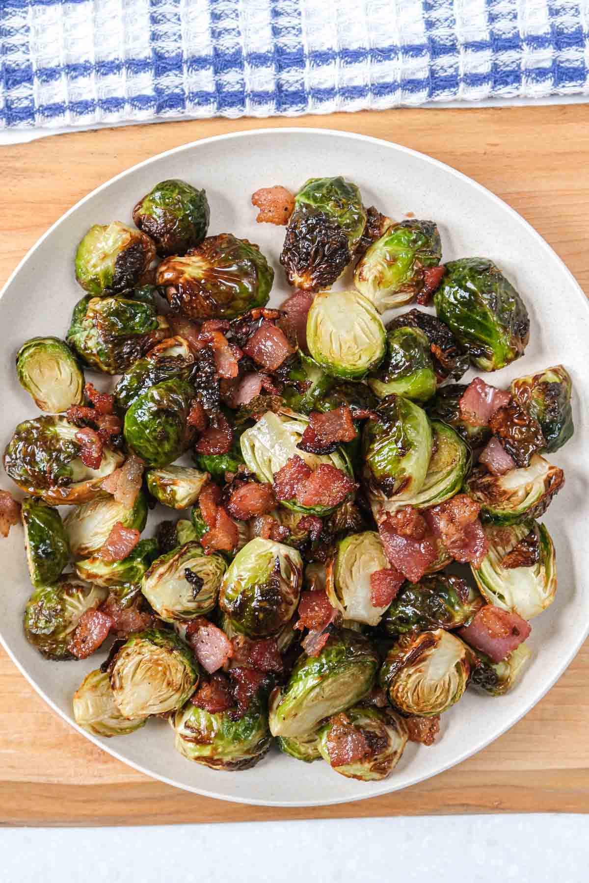 round white plate with crispy brussels sprouts and bacon on it sitting on wooden board.