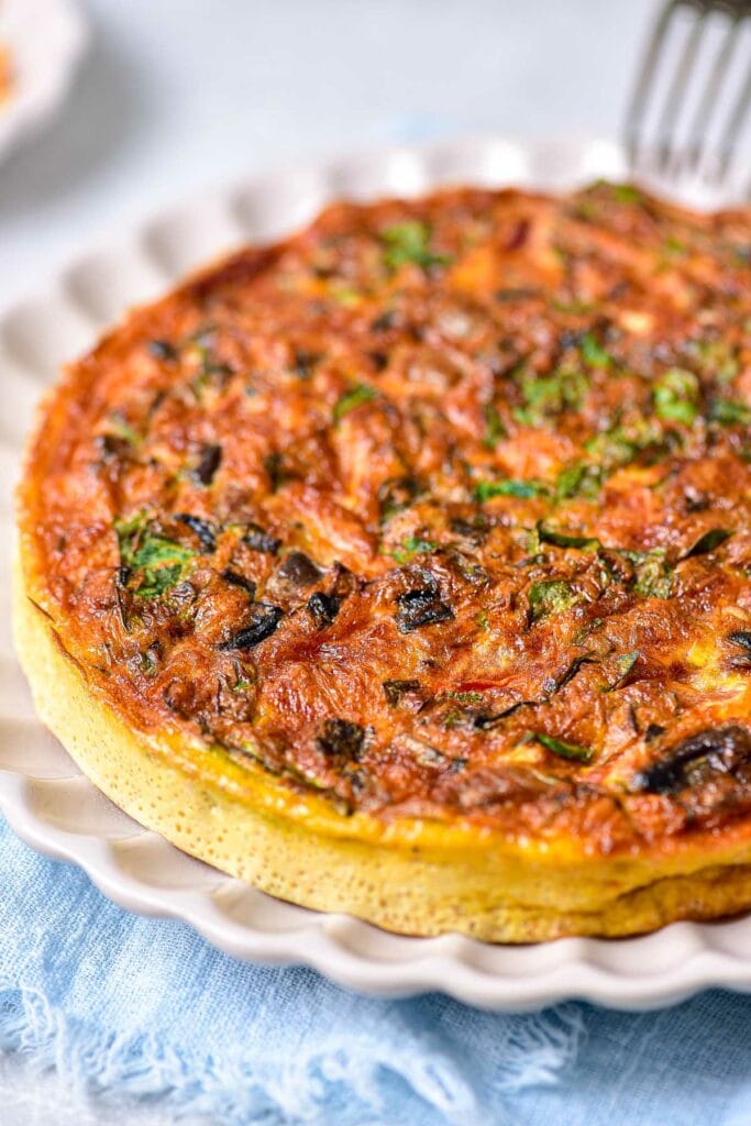 large round frittata on plate with fork above.
