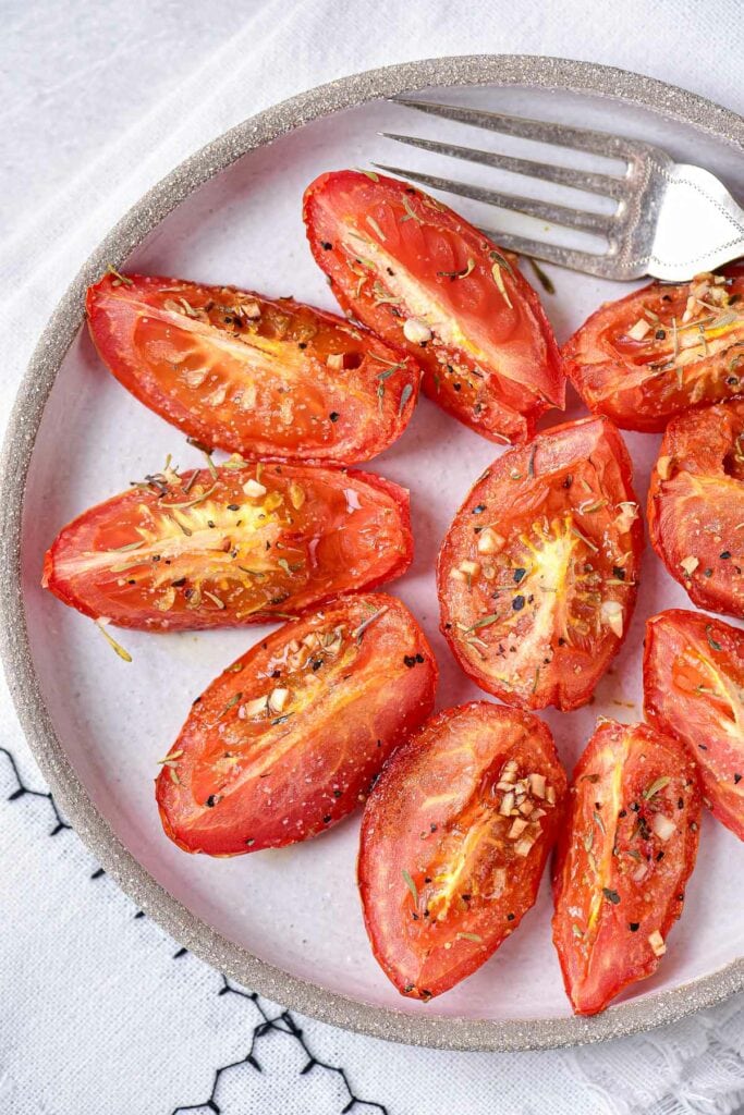 roasted tomato wedges on grey plate with silver fork beside.