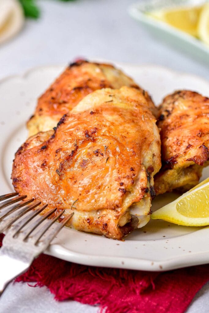 crispy chicken thighs on plate with silver fork and wedge of lemon beside.