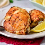 lemon chicken thighs on plate with lemon wedge and silver fork beside.