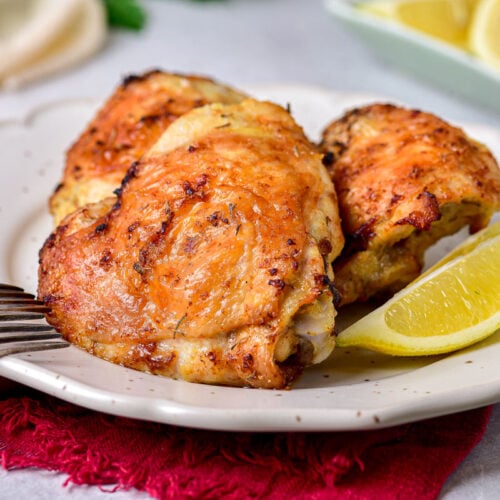 lemon chicken thighs on plate with lemon wedge and silver fork beside.