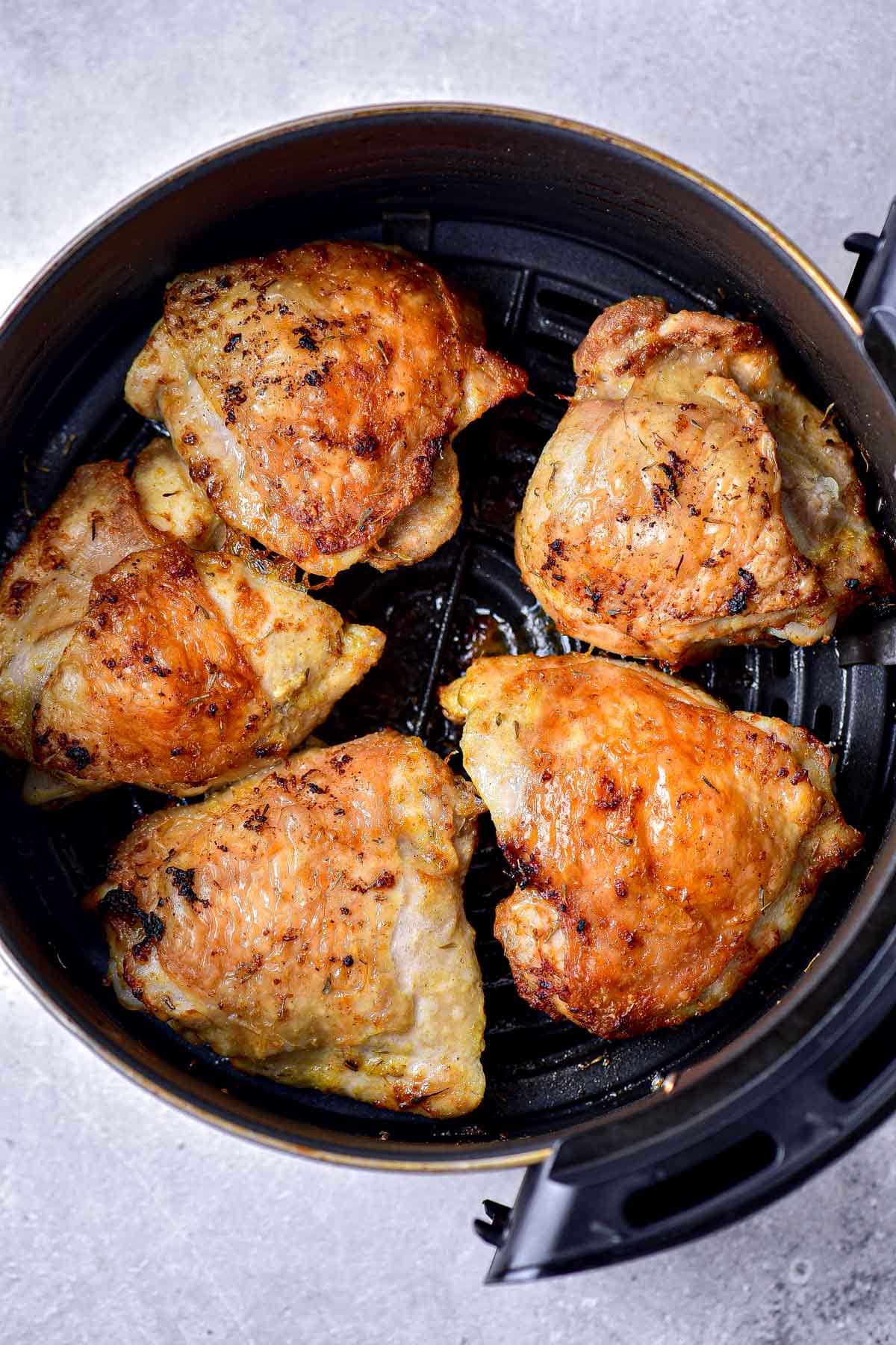 crispy lemon chicken thighs in round black air fryer tray sitting on counter.