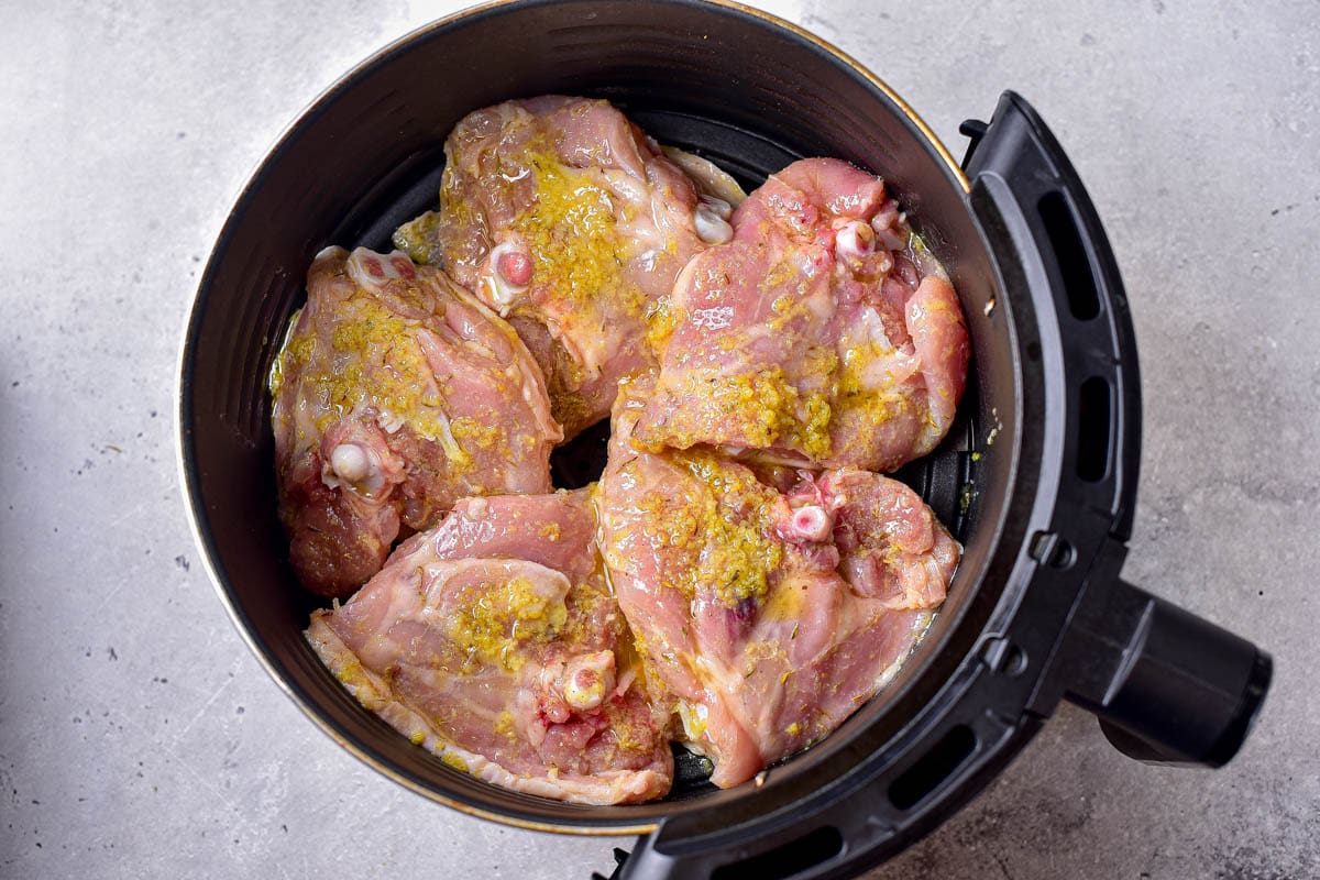 chicken thighs upside down in round black air fryer tray on counter.