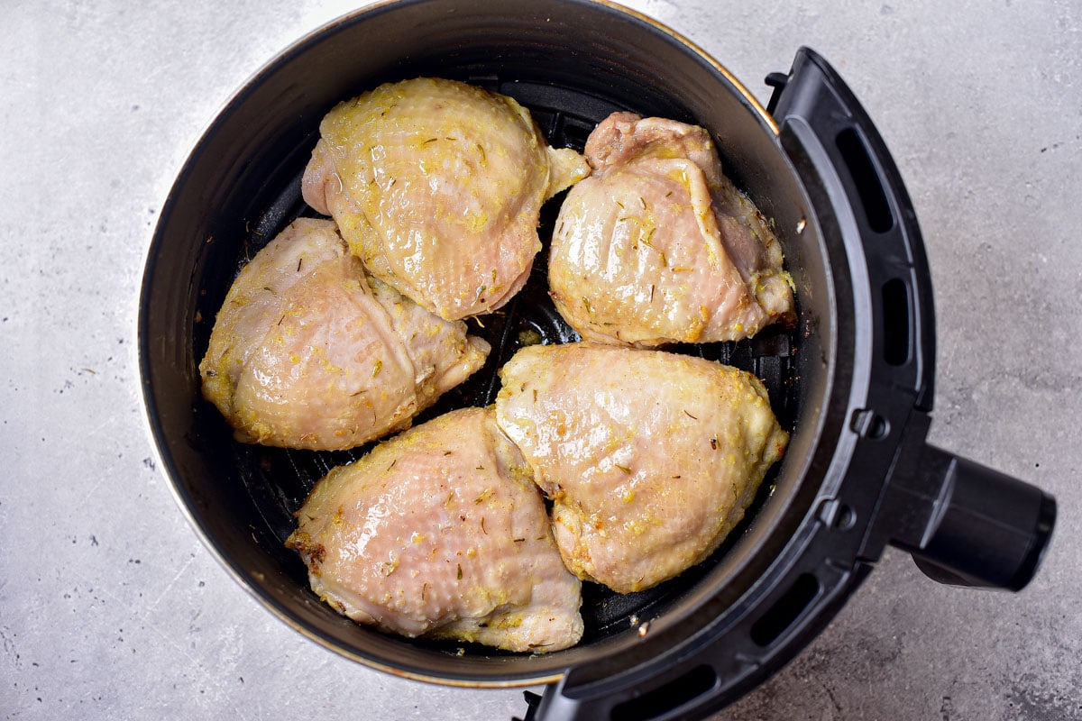 semi-cooked chicken thighs in round black air fryer basket on counter.