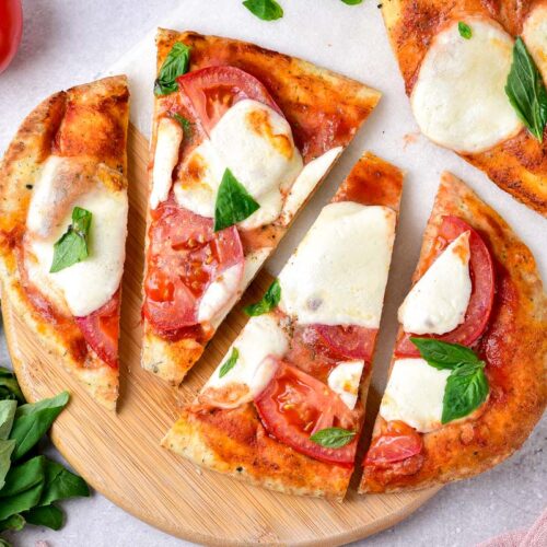 naan pizza cut into triangles sitting on cutting board.