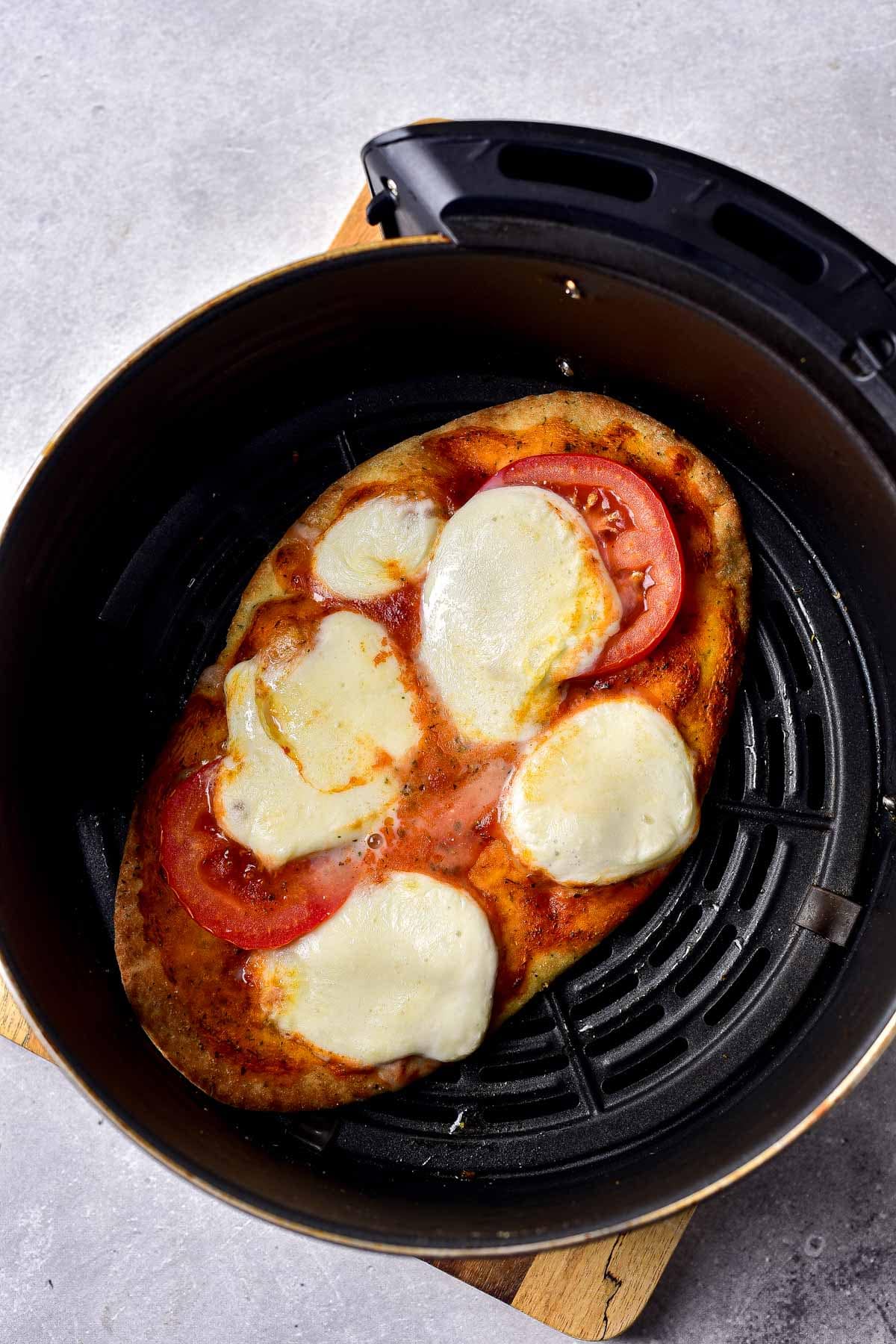 cooked naan pizza in round black air fryer tray on counter.