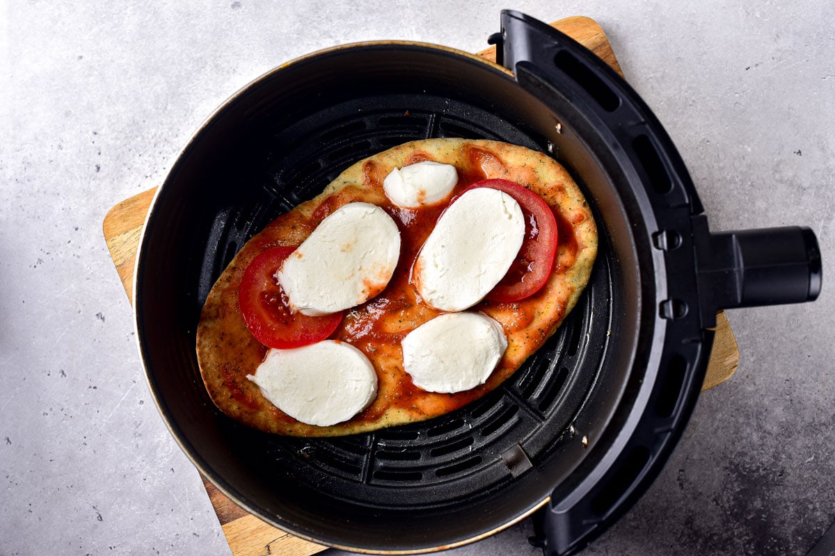 naan bread in air fryer with slices mozzarella and tomato sauce on it.