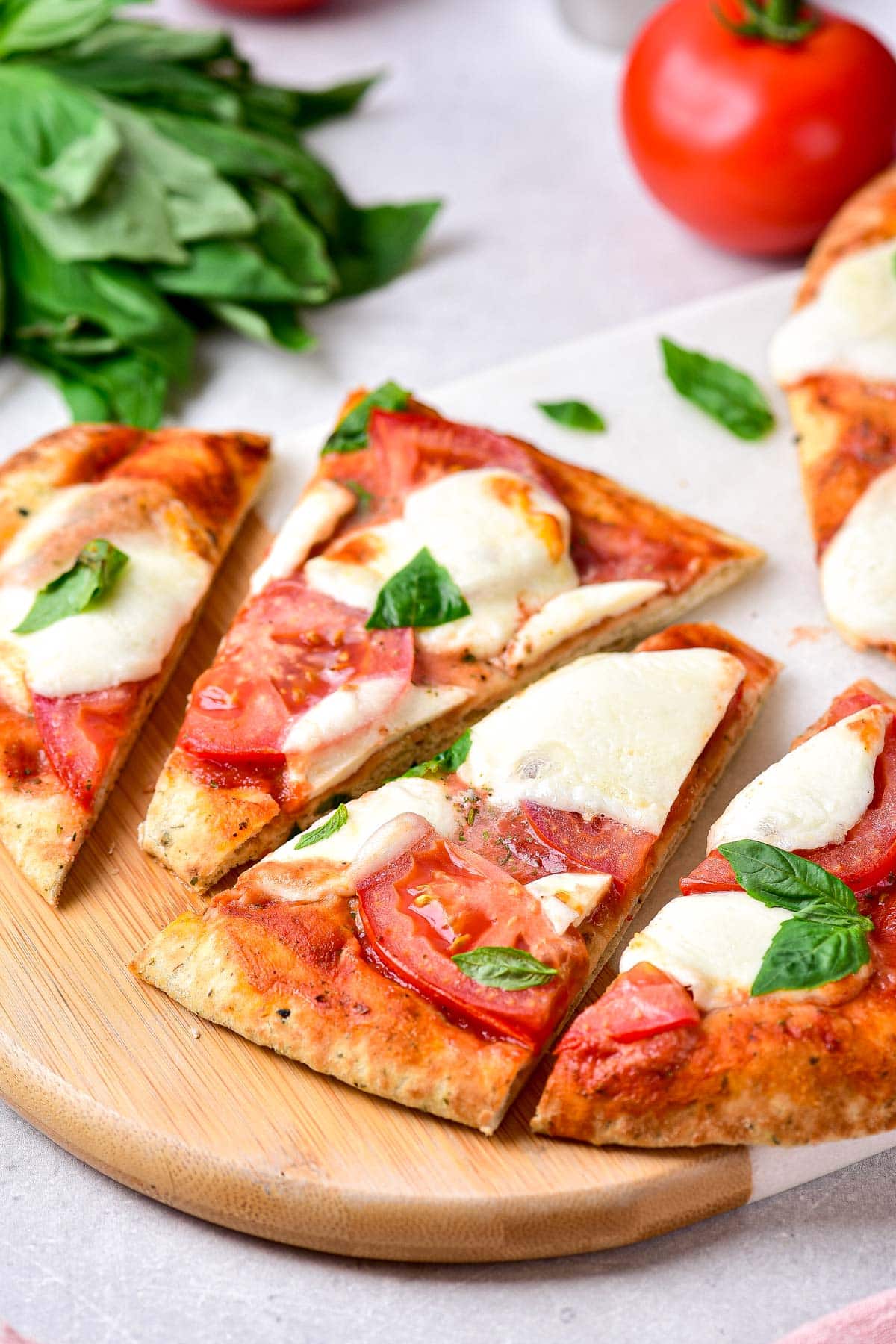 triangles of naan pizza sitting on cutting board with ingredients around on counter.