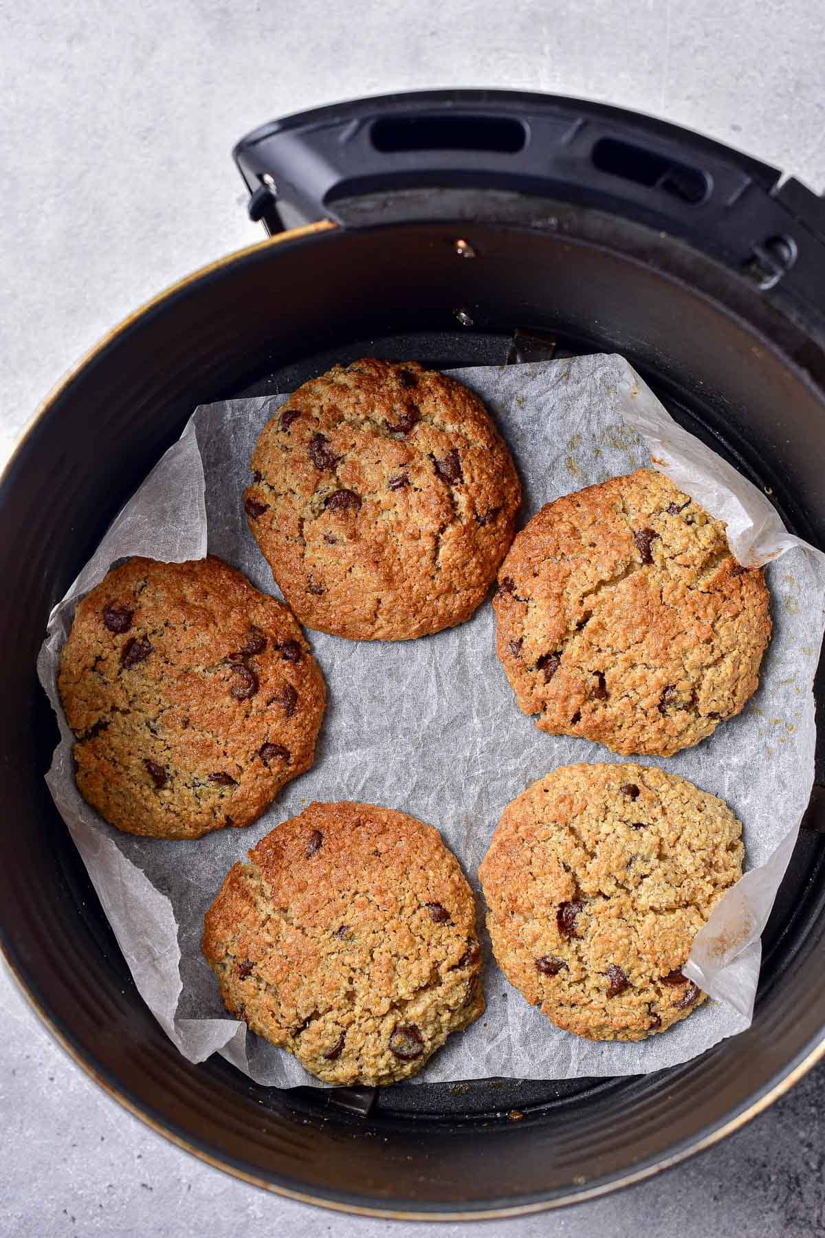crispy oatmeal cookies on parchment paper in round black air fryer basket.