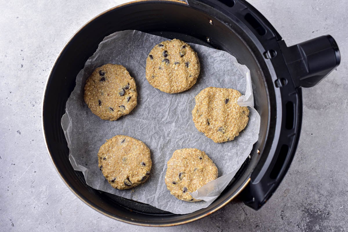 raw oatmeal cookies in air fryer basket lined with parchment paper.