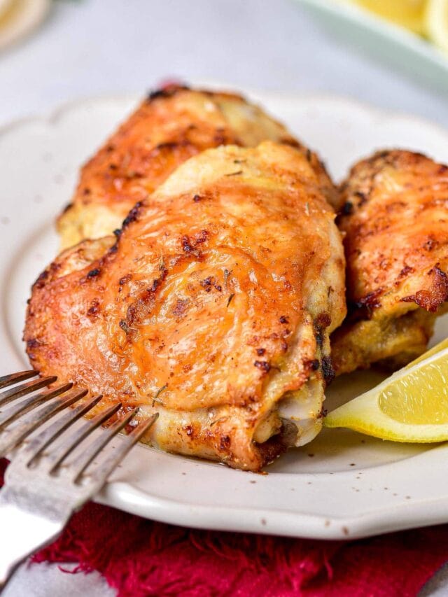 crispy chicken thighs on plate with silver fork and wedge of lemon beside.
