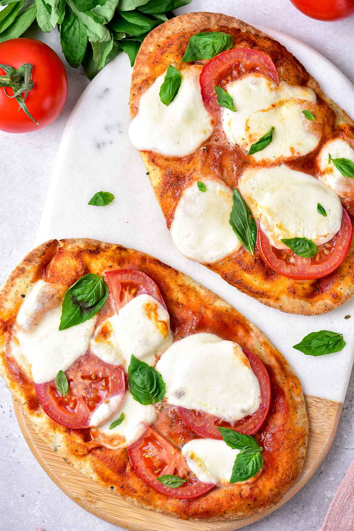 two crispy naan pizzas on cutting board sitting on counter.