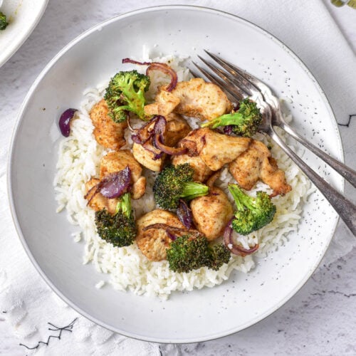 white plate of rice covered in chicken and rice with two forks beside.