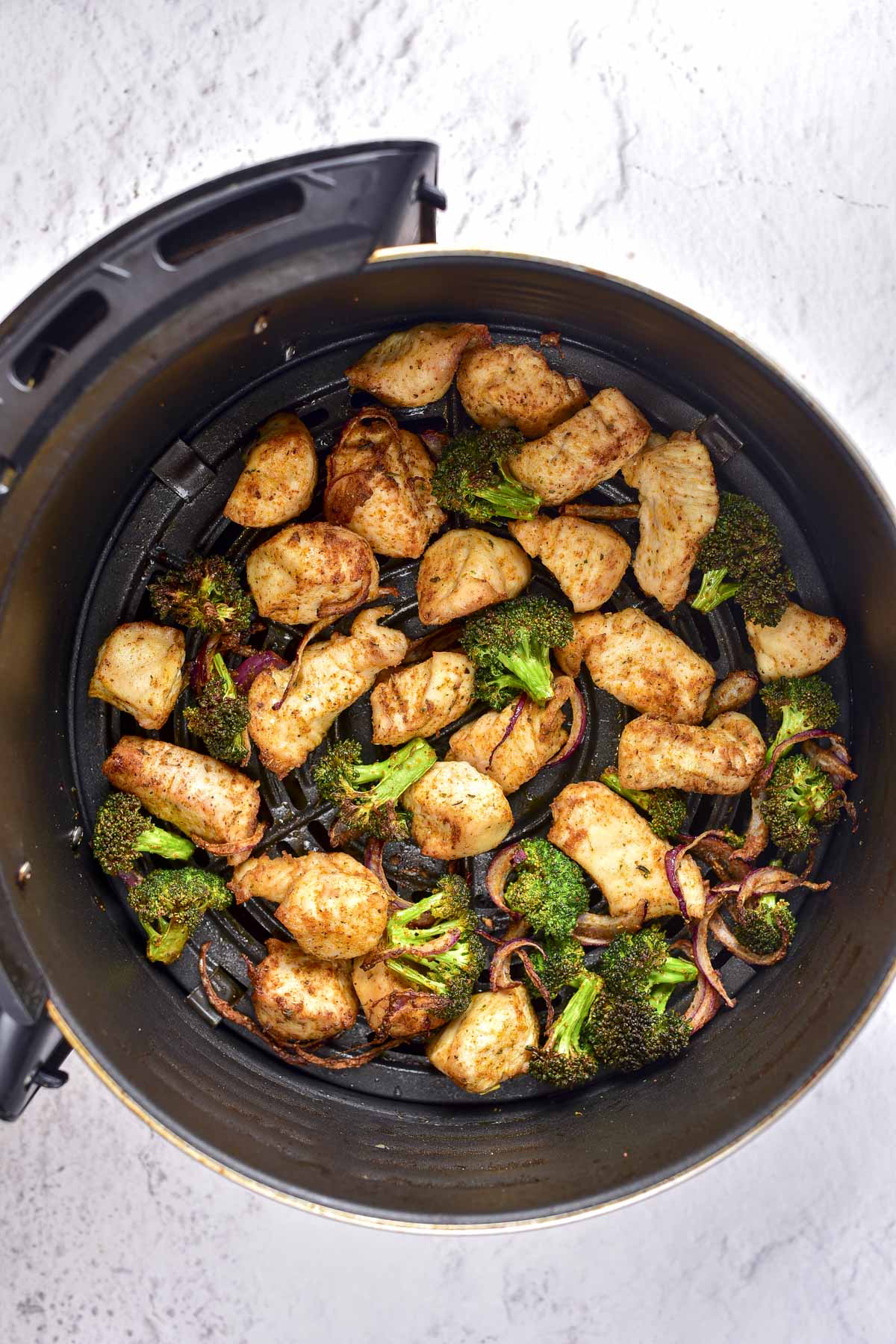 cooked chicken and broccoli in round black air fryer basket on counter.